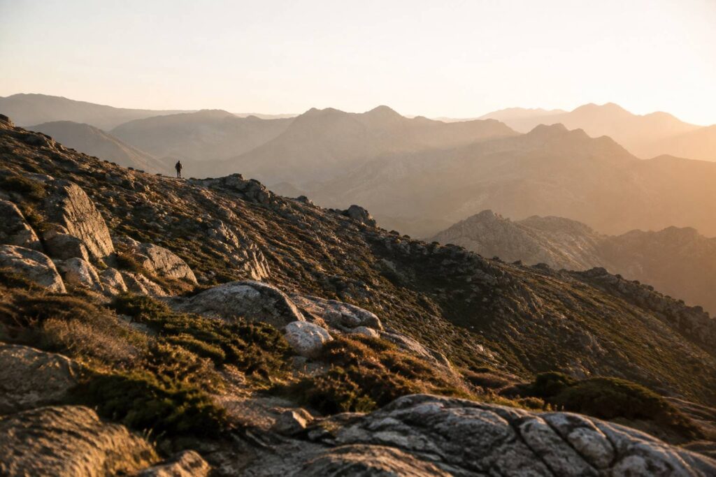 sentier de montagne escarpé en Corse traversant des crêtes rocheuses, un unique coureur de trail